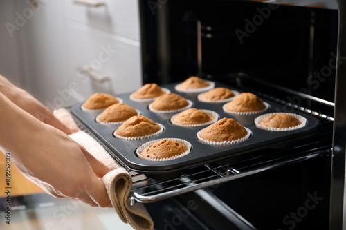 Tableau sur toile Woman taking baking tray with cupcakes from oven