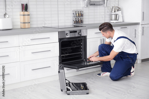 Young man repairing oven in kitchen