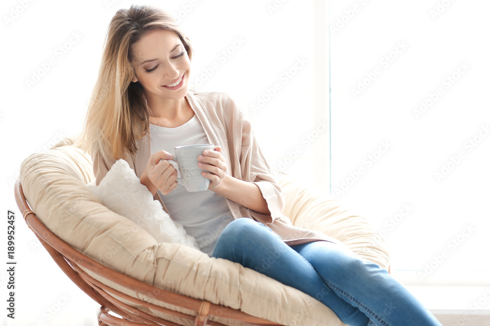 Happy young woman drinking tea while sitting in armchair at home Happy young woman drinking tea while sitting in armchair at home