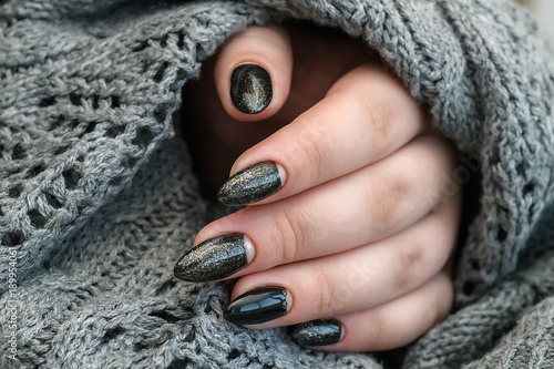 Beautiful winter manicure. Black lacquer with luster and white patterns of snow and frost. The gray background is also with beautiful curled drawings photo