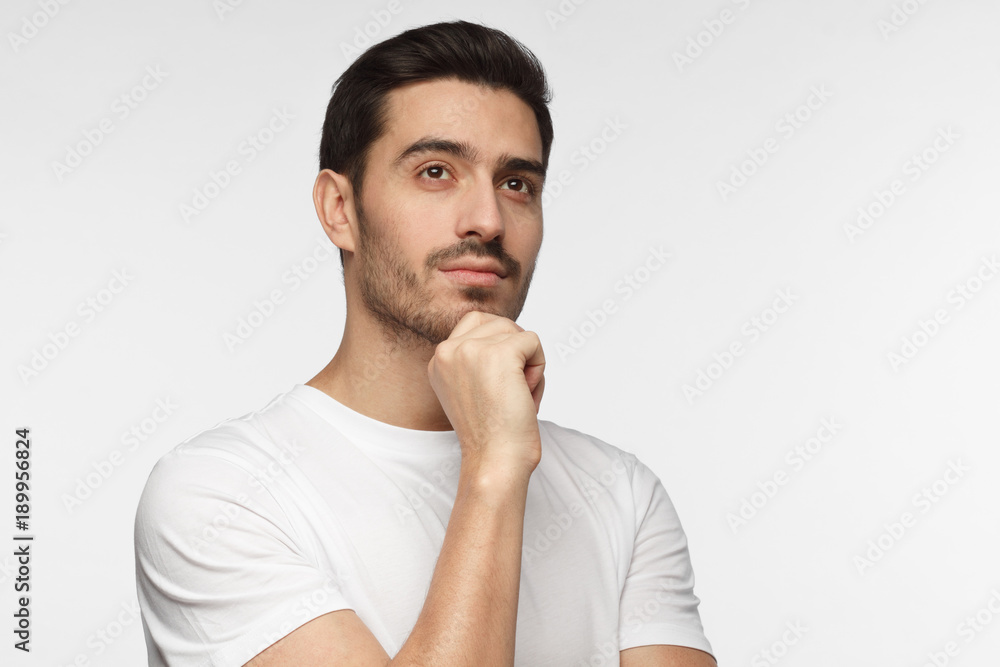 Portrait of young man with dreamy cheerful expression, thinking, isolated over gray background with copy space for your text Portrait of young man with dreamy cheerful expression, thinking, isolated over gray background with copy space for your text