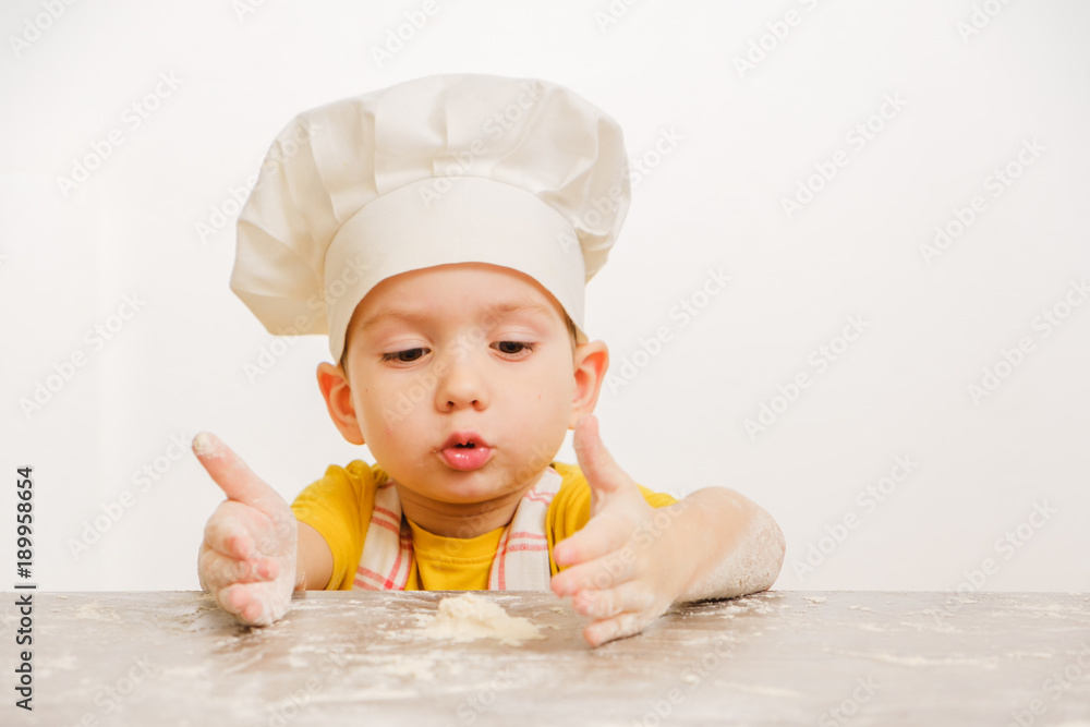 Details of children's hands kneading dough. Cheerful cook child boy in a cap prepares burritos Details of children's hands kneading dough. Cheerful cook child boy in a cap prepares burritos