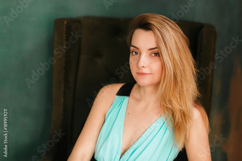 Portrait of the beautiful woman sitting in a chair and looking straight. Close-up shot. Loft green wall on background.
