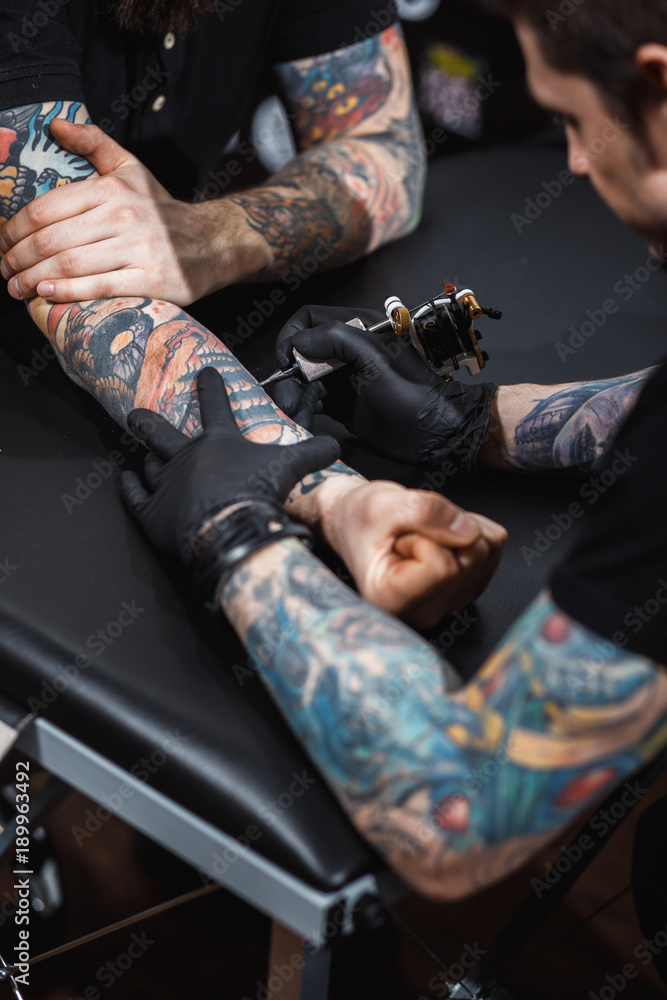 master tattooist makes a tattoo on the skin of the client with special equipment