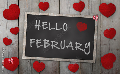 Blackboard with words hello february, surrounded by red hearts, on vintage wooden background photo