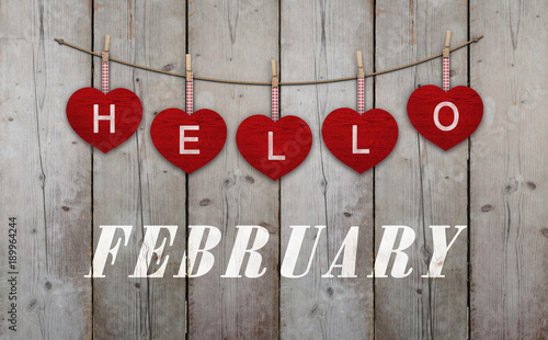 Hello february written on hangingred hearts and weathered wooden background photo