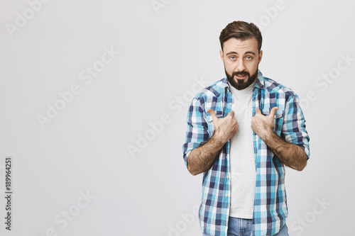 Fotografija Studio shot of bearded european person pointing at himself with offended expression, standing against gray background