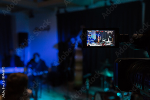 LCD display on the camcorder. Filming of the concert. Musicians playing the double bass, synthesizer, guitar and percussion.