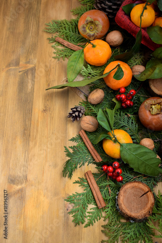 Winter composition consisting of thuja branches  berries  persimmon  mandarins  nuts and cinnamon sticks. Copy space