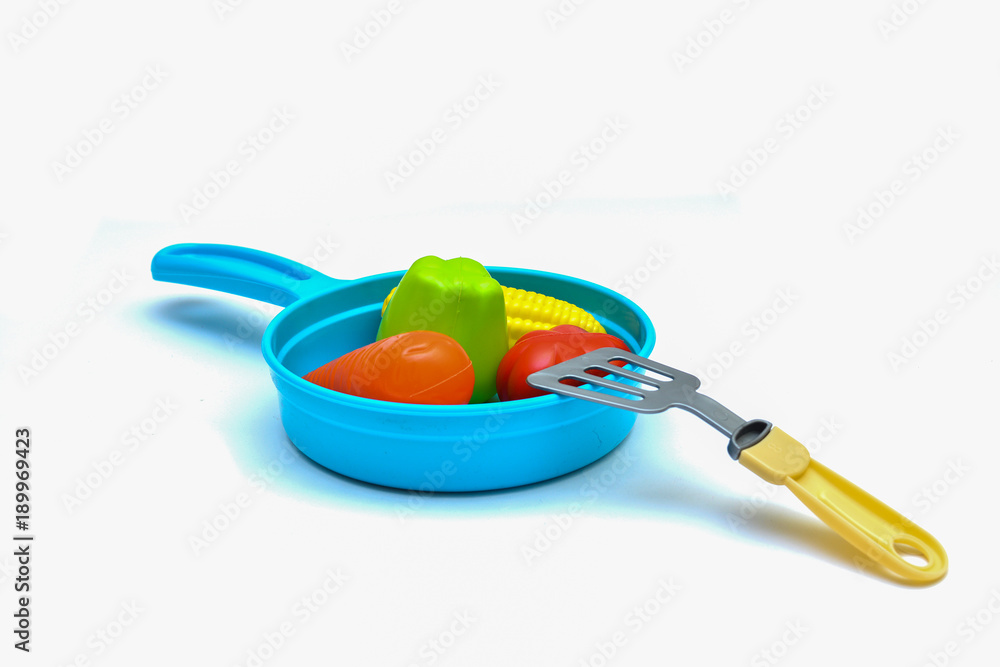 Children's toys - a plastic frying pan, vegetables and a scapula on a white background. Children's toys - a plastic frying pan, vegetables and a scapula on a white background.