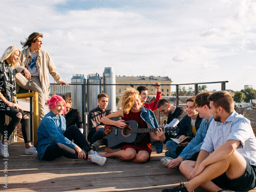 Fotka „Relaxed smiling young people travel Europe. Sitting on a rooftop  singing and enjoying their trip. Youth lifestyle“ ze služby Stock | Adobe  Stock