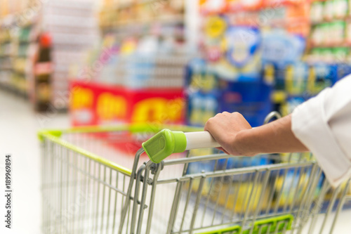 Woman pushing shopping cart in supermarket store abstract blur background with shopping cart, Supermarket aisle with empty shopping cart