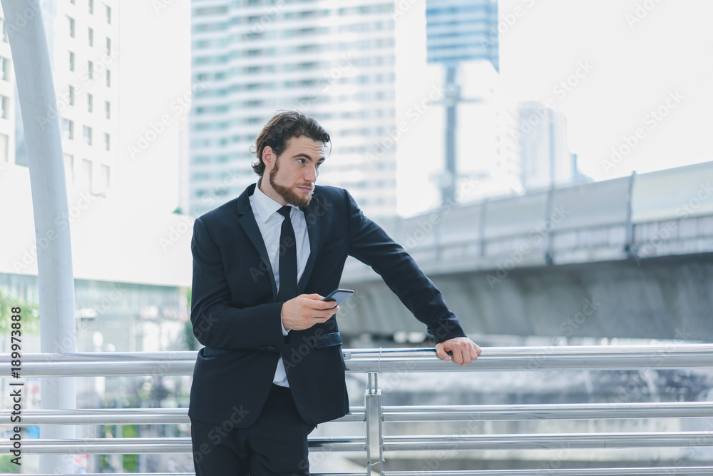 Smart businessman in full suit standing outdoors using smartphone for manage business project in cityscape background Smart businessman in full suit standing outdoors using smartphone for manage business project in cityscape background