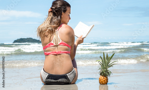beautiful girl sitting on the beach and reading a book on exotic landscapes and pineapple photo