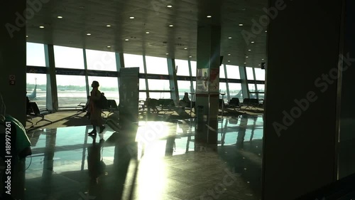airport terminal interior, people travellers passengers silhouettes waiting in a lounge, hall view, beautiful background with sunshine, dolly shot from escalator