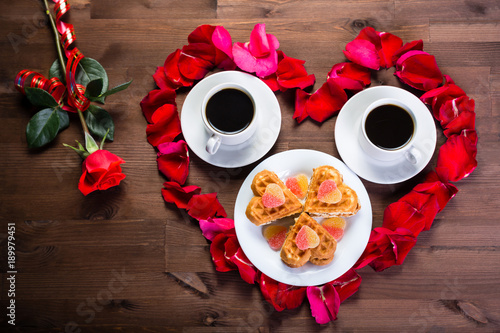 On the table lies a rose next to the heart of the lepidopter roses within which are two cups of coffee. photo