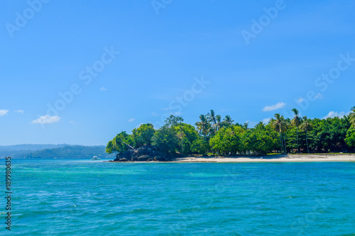Wunderschöne tropische Insel inmitten vom Meer umgeben, grüne Bäume und Palmen, weißer Sandstrand, blaues Wasser und blauer Himmel, Karibik, Samana, Dominikanische Republik