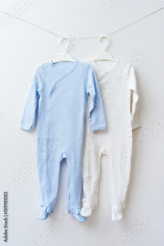 Two baby onesies on hangers. Blue and white baby pajamas on hanger. 