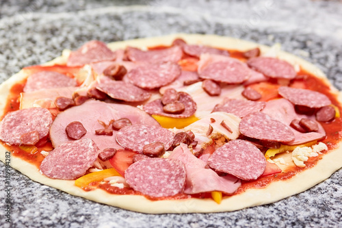Unbaked pizza with many sliced sausages close up. Pizza with sliced cold meat products.