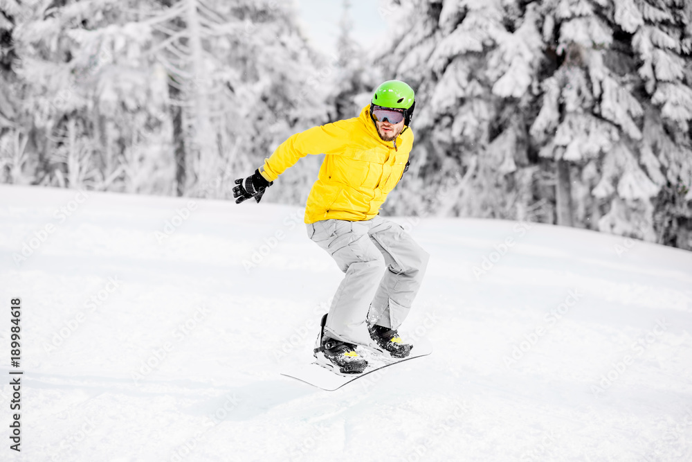 Man in colorful sports clothes riding the snowboard on the snowy mountains with beautiful trees on the background