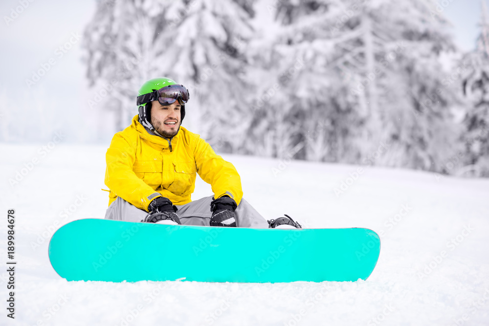 Man sitting with snowboard resting after the riding outdoors at the snowy mountains Man sitting with snowboard resting after the riding outdoors at the snowy mountains