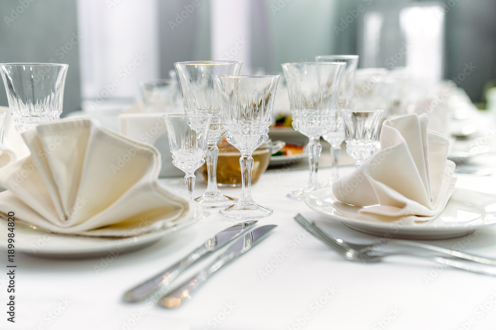 Luxury dinner set arranged on a table with vintage cream lace tablecloth and napkins, elegant porcelain dishes, silverware and crystal glassware