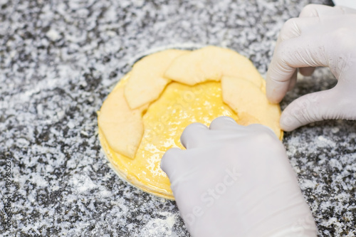 Hands putting apple slices to round greased dough. Adding ingredients to apple tart. Apple tart cooking. photo