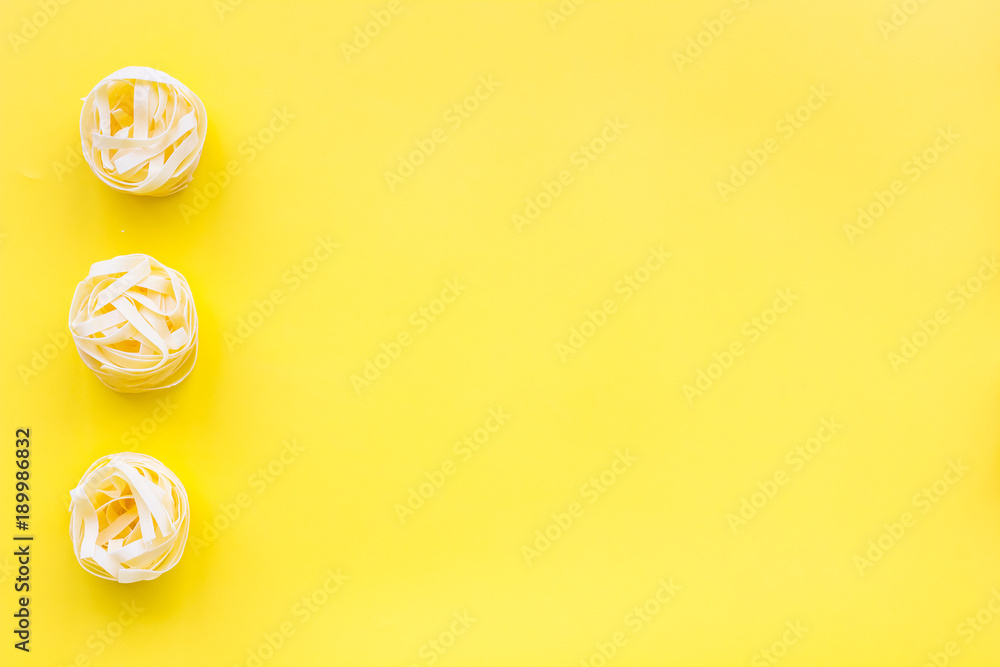 Fototapeta Uncooked tagliatelle. Italian pasta. Pattern on pastel yellow background top view copy space