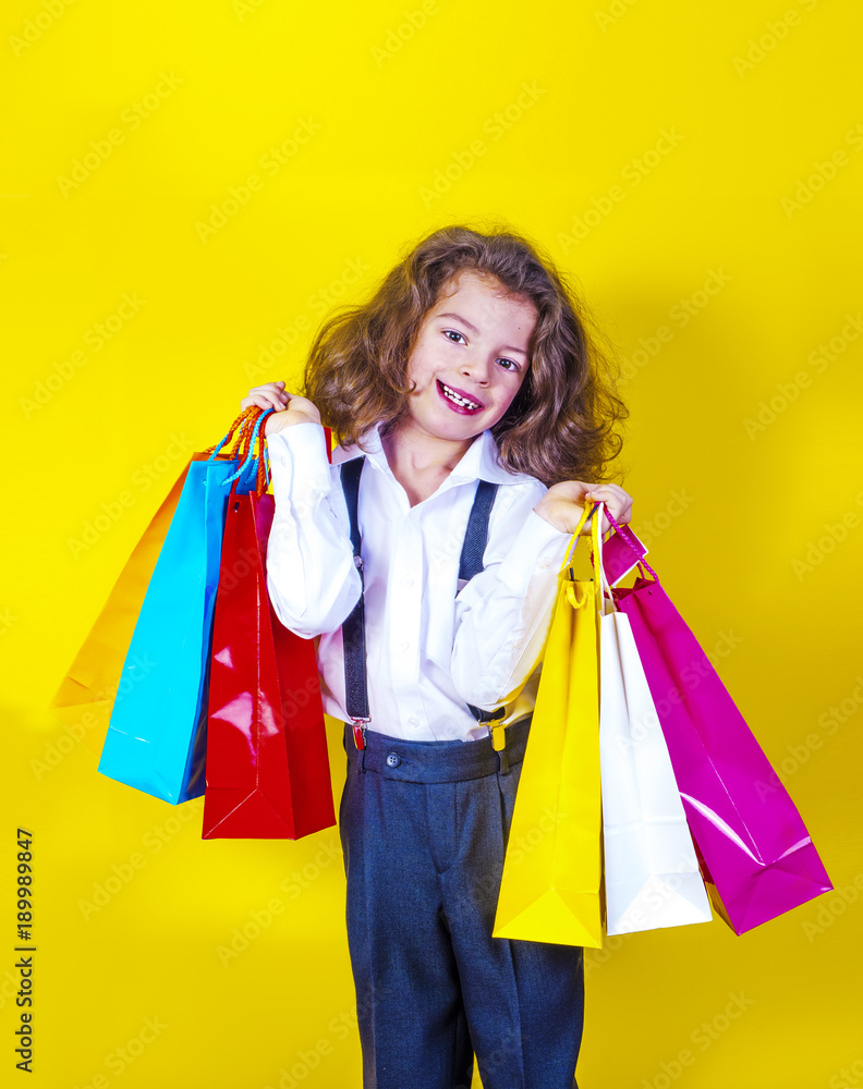 Happy little boy with shopping bags. Isolated on a yellow background