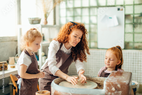 young mother and two redhead daughters made clay cup with pottery wheel photo
