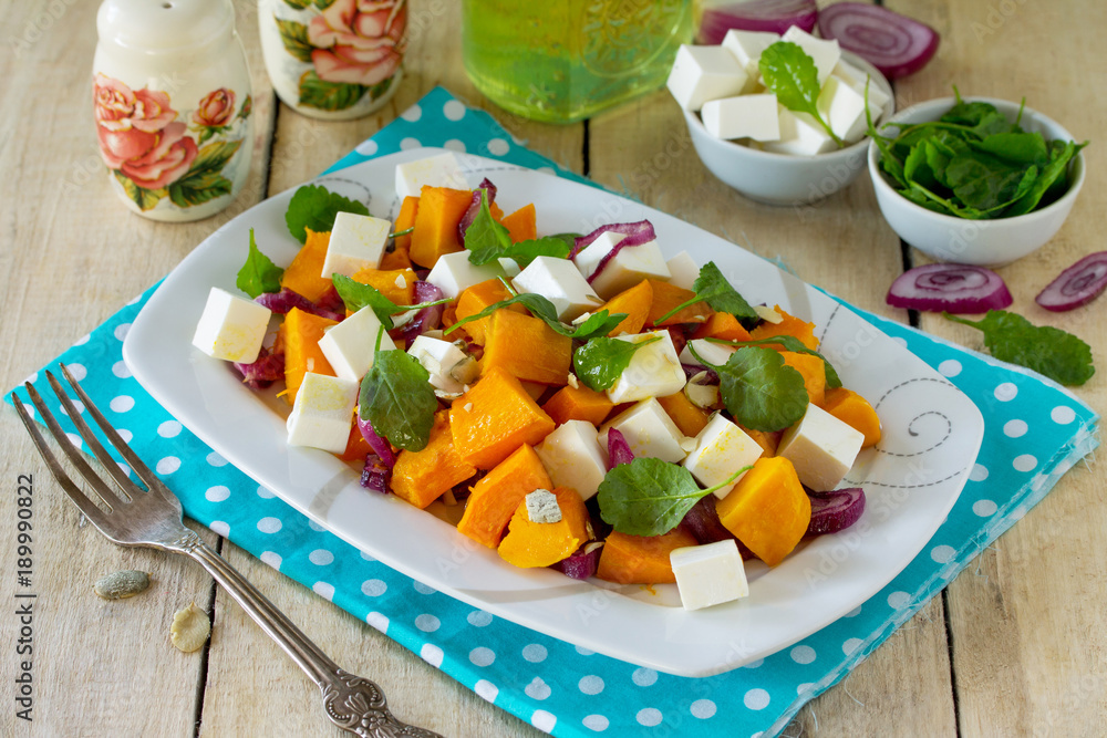 Warm pumpkin salad with onions, served with feta cheese, arugula and pumpkin seeds on a rustic table. The concept of healthy eating. Warm pumpkin salad with onions, served with feta cheese, arugula and pumpkin seeds on a rustic table. The concept of healthy eating.