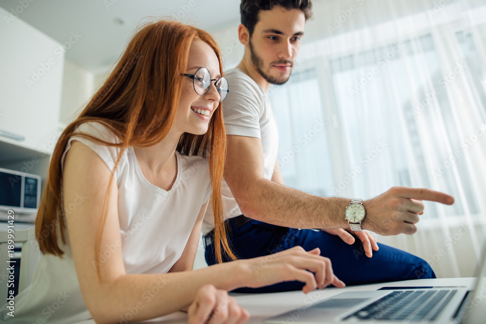 Happy couple with laptop spending time together at home, man pointing at screen Happy couple with laptop spending time together at home, man pointing at screen