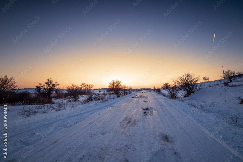 Winter sunset landscape with trees and field road.