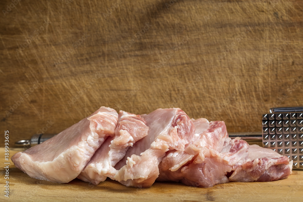 Slices of fresh pork sirloin meat with a metallic hammer for beating meat Slices of fresh pork sirloin meat with a metallic hammer for beating meat