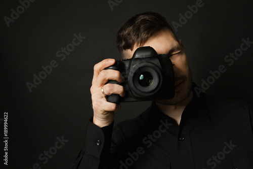 Man with camera in hands in black shirt on black background © alexbutko_com