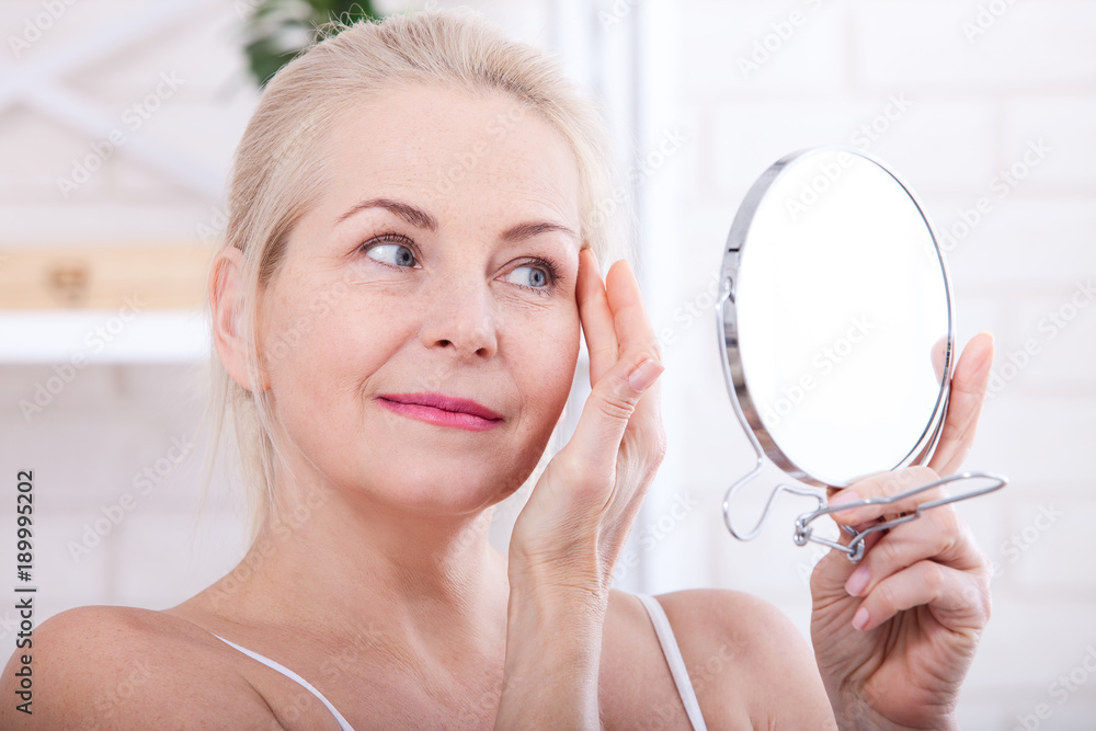 Middle aged woman looking at wrinkles in mirror. Plastic surgery and collagen injections. Makeup. Macro face. Selective focus Middle aged woman looking at wrinkles in mirror. Plastic surgery and collagen injections. Makeup. Macro face. Selective focus
