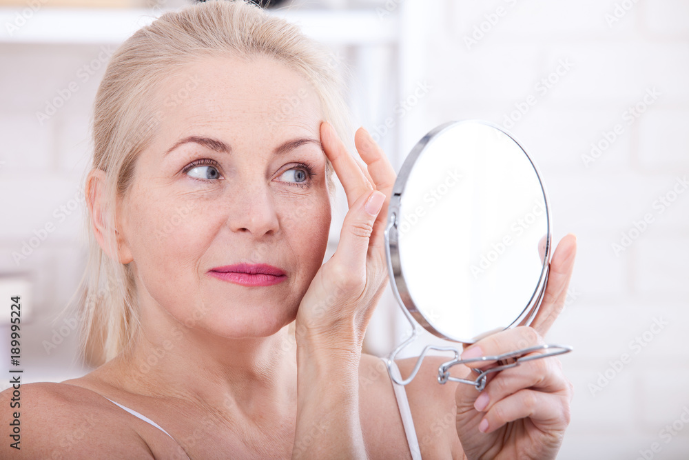 Middle aged woman looking at wrinkles in mirror. Plastic surgery and collagen injections. Makeup. Macro face. Selective focus Middle aged woman looking at wrinkles in mirror. Plastic surgery and collagen injections. Makeup. Macro face. Selective focus