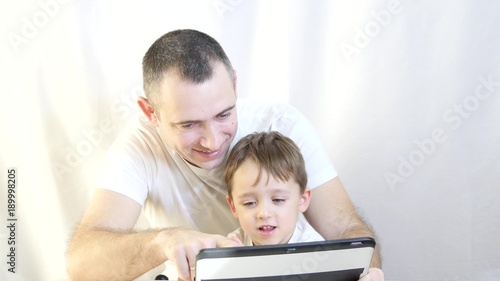 father and son are sitting at the table and playing with a tablet on a white background. The concept of a happy family - 2