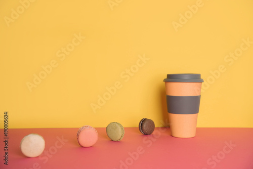 Cup of coffee to go with macaron on yellow and pink background