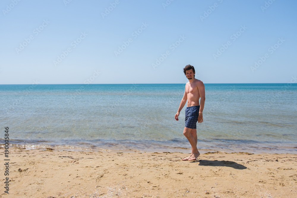 A man in a blue suit with a beard walks on the beach.