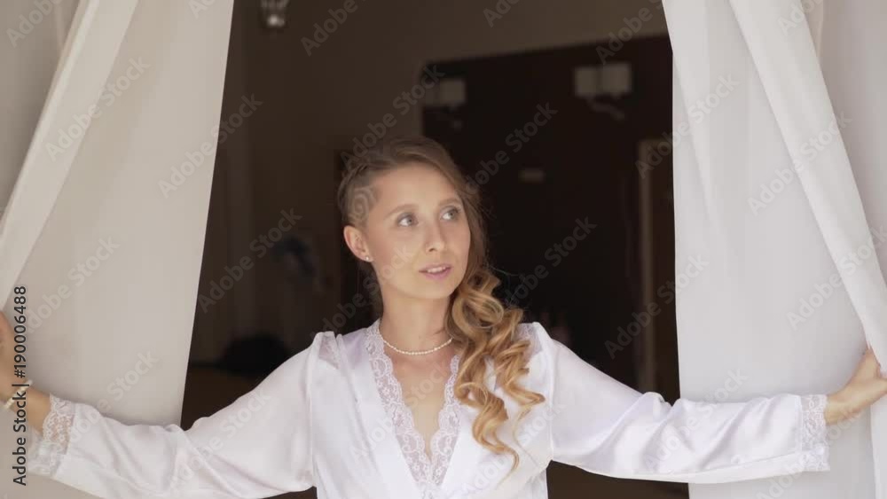 Morning of the bride. A girl in a robe opens the curtains Morning of the bride. A girl in a robe opens the curtains