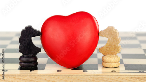 two chess knights black and white are kissing the red heart between them on the chess board