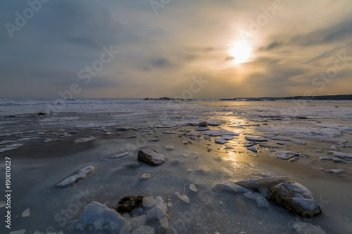 Stones  ice floes and a frozen sea in the sun s rays at sunset. Winter landscape