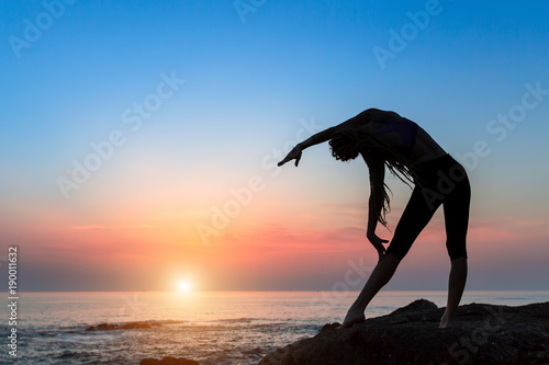 Yoga woman silhouette on the sea during amazing sunset. Fitness exercises and healthy lifestyle.