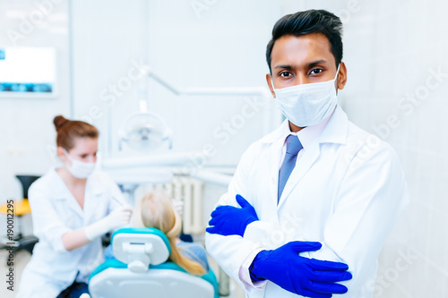 Portrait of a young confident asian male dentist in clinic in front of wfemale dentist checking teeth to patient. Dental clinic concept