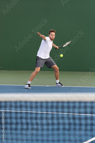 Professional tennis player athlete man hitting forehand ball over net on hard court playing tennis match. Sport game fitness lifestyle. © Maridav