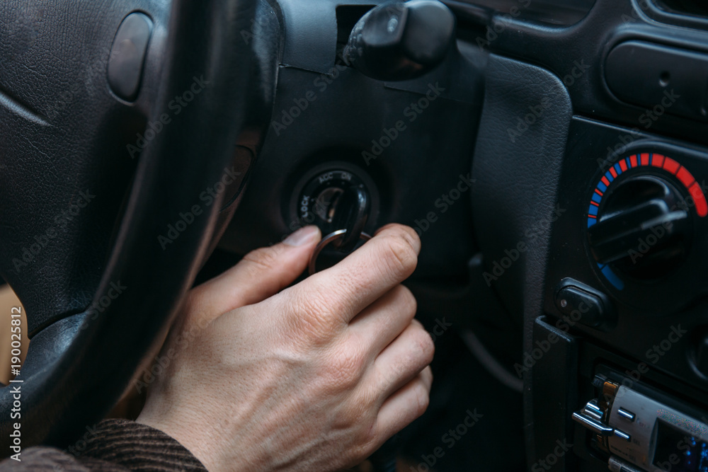 male driver hand inserts key in ignition lock to start car