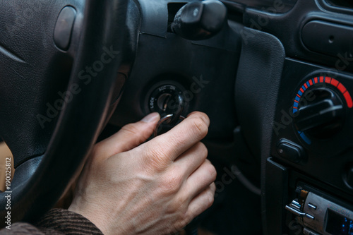 male driver hand inserts key in ignition lock to start car © DedMityay