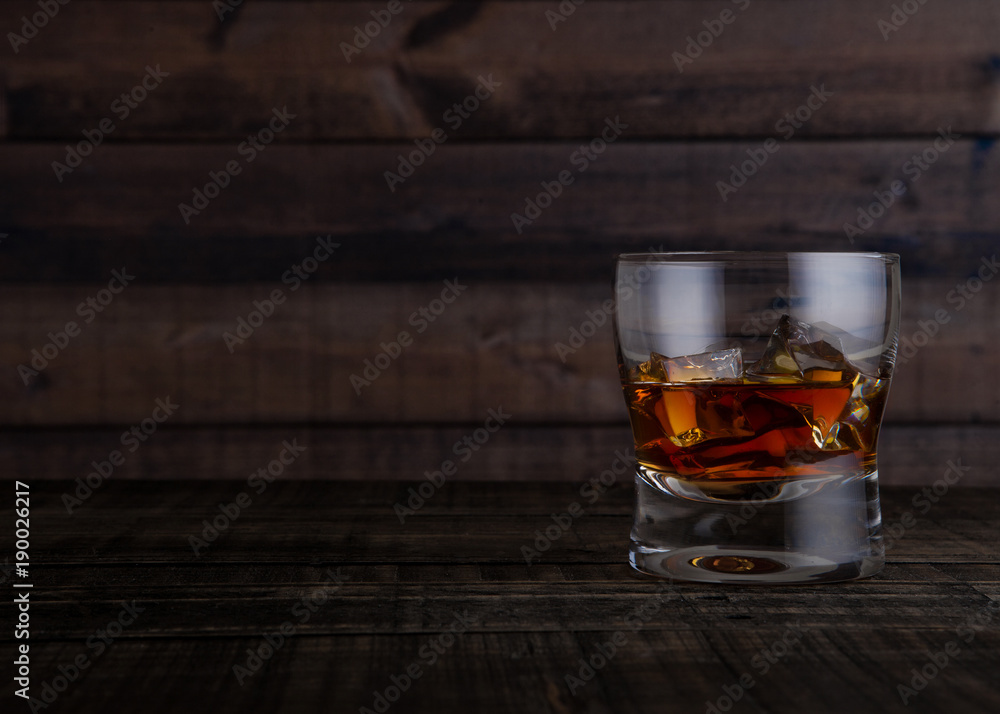Glass of whiskey with ice cubes on wooden table Glass of whiskey with ice cubes on wooden table