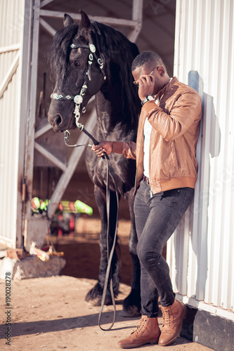 african Man wearing sunglasses near a black horse in hangar photo